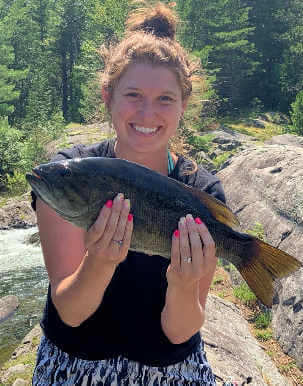 Happy young lady angler holding nice smallmouth bass.